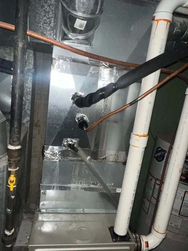 Sheet metal trunk duct running along a basement ceiling beside plumbing lines.