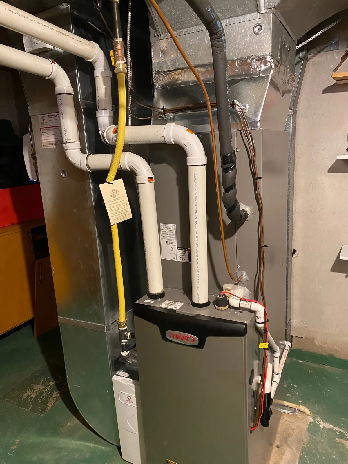 White PVC intake and exhaust vent pipes and a yellow gas line on a high-efficiency furnace