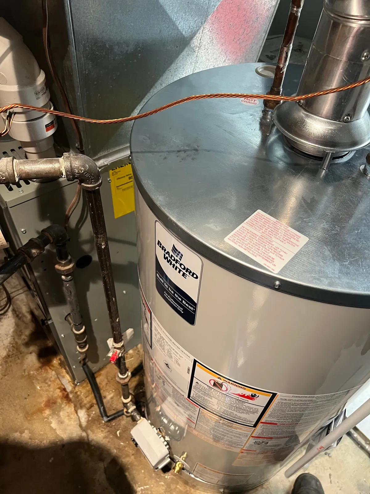 Hot water tank in a basement with the gas valve and the water piping visible above it.