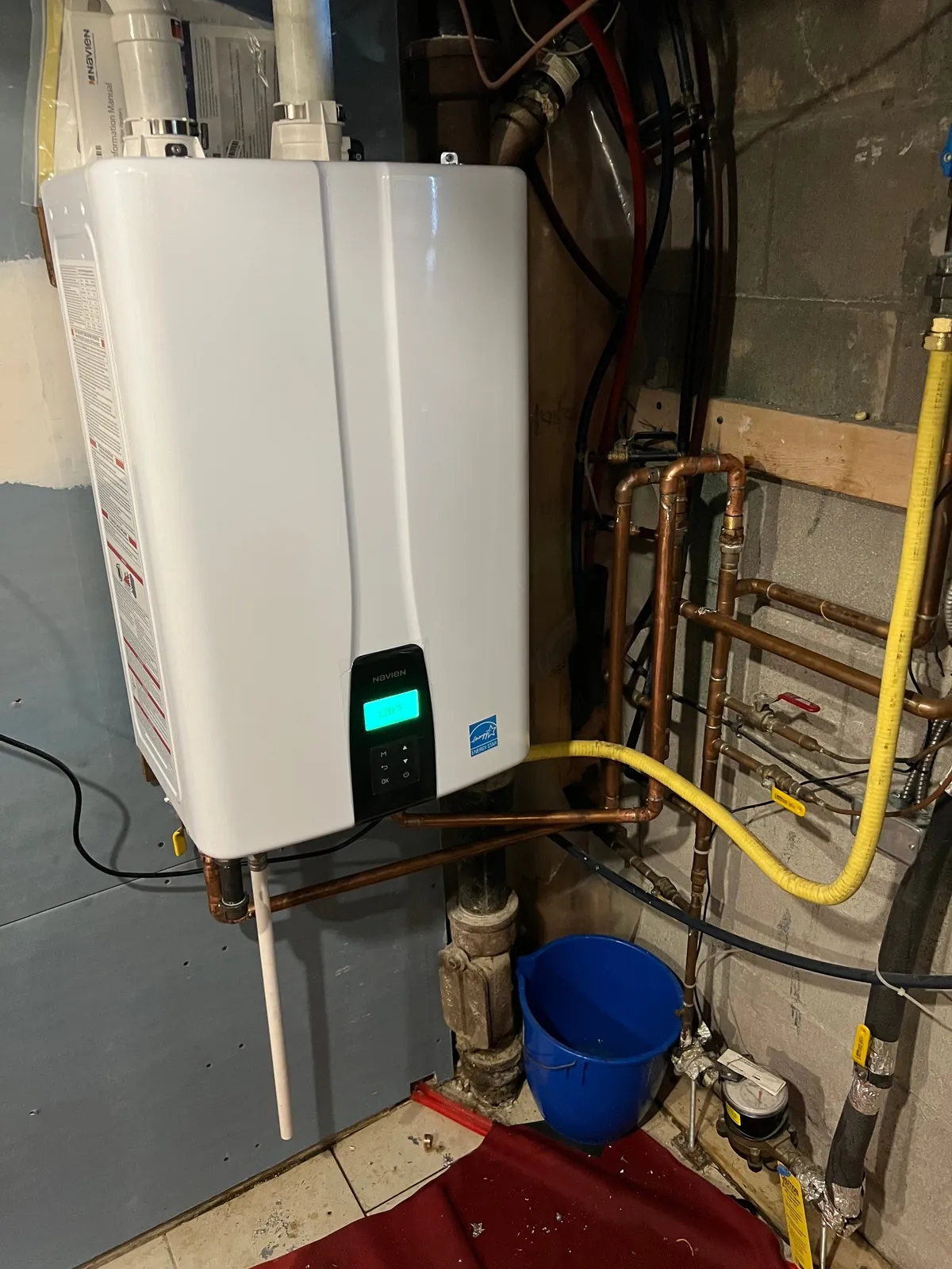 Wall-hung tankless water heater with the gas and water connections run below it in a basement.