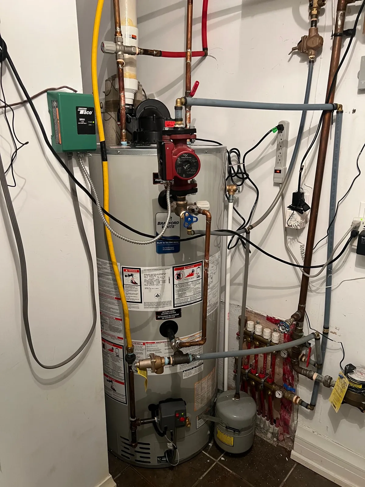 Hot water tank with a recirculation pump and copper piping above it in a basement.